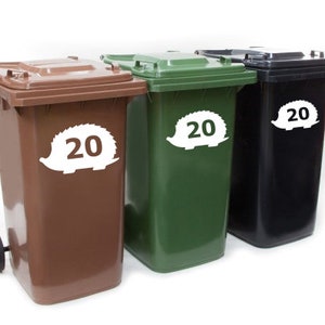 Puede incluir: Tres cubos de basura de 20 galones con pegatinas de erizo. Los cubos son marrones, verdes y negros.