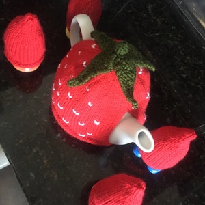 Puede incluir: Un juego de cuatro fundas de tetera de punto de fresa. Las fundas son rojas con semillas blancas y hojas verdes. Las fundas están diseñadas para adaptarse a una tetera y tres tazas de té.