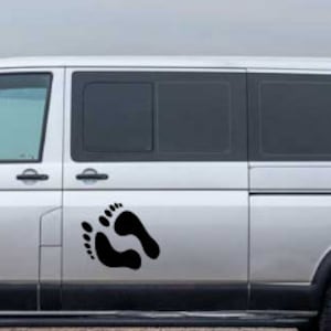Op de afbeelding: Een zilveren bestelwagen met een zwarte voetafdruk sticker op de zijdeur.