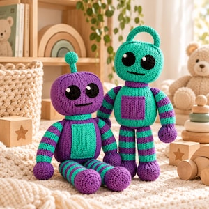 May include: Two knitted robot toys featuring purple and teal yarn. One robot is seated with a small antenna on its head, while the other stands upright with a loop on top. Both have large black circular eyes, simple stitched mouths, and square chest panels.