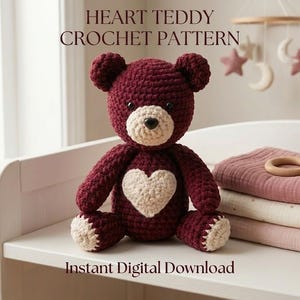 May include: A dark maroon crochet teddy bear with a cream-coloured heart on its chest, cream muzzle, and cream paw pads. The text HEART TEDDY CROCHET PATTERN and Instant Digital Download are visible. The bear has black safety eyes and a black nose.