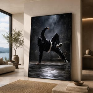 May include: A framed wall art print featuring a person in a black hooded sweatshirt and black pants performing a breakdance move on a dark, textured floor against a smoky, dark background with dramatic lighting and high contrast.