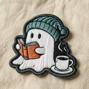May include: An embroidered patch featuring a white ghost wearing a teal knit beanie, reading an orange book, and sitting next to a steaming white cup of coffee on a saucer. The design is outlined in black thread with detailed stitching.