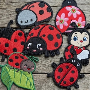 May include: A collection of seven embroidered ladybug patches featuring various designs, including a ladybug on a green leaf, a heart-shaped ladybug, a ladybug with pink flowers, and several cartoon-style ladybugs with black spots and red wings.