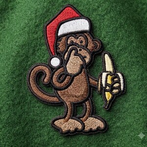 May include: An embroidered patch featuring a brown monkey wearing a red and white Santa hat. The monkey has one hand raised to its mouth in a shushing gesture and holds a yellow banana in the other hand. The patch has a thick black border.