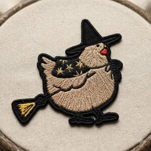 May include: An embroidered patch featuring a light brown chicken wearing a black witch hat and a black cape adorned with gold stars. The chicken is depicted holding a yellow broomstick, with the entire design outlined in black thread.