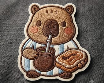 Può includere: Una toppa ricamata raffigurante un capibara marrone che indossa una camicia a righe azzurre e bianche. Il capibara tiene in mano un contenitore per mate marrone scuro con una cannuccia bombilla argentata e una fetta di pane tostato.