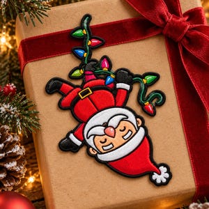 May include: An embroidered patch featuring a cartoon Santa Claus hanging upside down while tangled in a string of colorful Christmas lights. The patch has a black border and depicts Santa with a red suit, white beard, and a red hat with a white pom-pom.