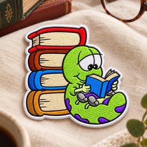 May include: An embroidered patch featuring a bright green cartoon caterpillar with purple spots sitting next to a stack of four colorful books. The caterpillar is holding and reading a small blue book. The patch has a white border.