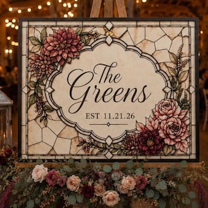 May include: A rectangular sign featuring a stained glass pattern with dark outlines. The center displays the text The Greens and EST 11.21.26 in black script and serif font. The corners are decorated with illustrations of red and pink flowers.