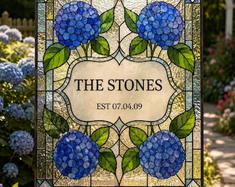 Può includere: Un pannello rettangolare in vetro colorato con quattro grappoli di ortensie blu e foglie verdi negli angoli. Il centro contiene una placca di vetro color crema con il testo nero THE STONES e EST 07.04.09. Il pannello è incorniciato in metallo scuro.