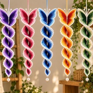 May include: Five hanging crochet butterfly wind spinners in purple, pink, blue, orange, and green. Each piece features a butterfly top with white antennae, a spiraling body with white scalloped edges, and a single white bead at the bottom.
