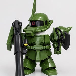 May include: A green plastic robot action figure with a large head and small body. The figure features a single red eye, a tall fin on its helmet, and a black bazooka in its right hand. It holds a black battle axe in its left hand.