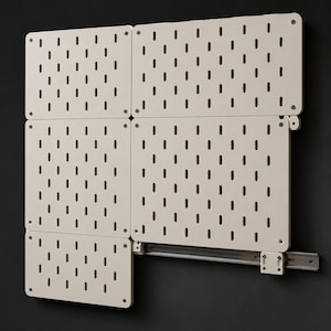 Puede incluir: Un sistema modular de tablero perforado para pared compuesto por cinco paneles rectangulares de color blanco roto con esquinas redondeadas y ranuras verticales. Los paneles están sujetos con tornillos visibles a un riel metálico horizontal.