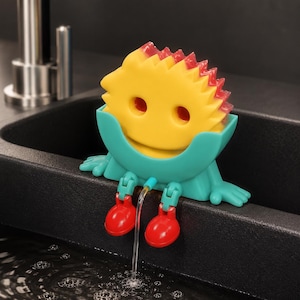 May include: A yellow and red spiky sponge with two eye holes sits inside a teal plastic holder. The holder features two teal arms resting on the edge and two dangling red legs with feet, with a thin stream of water flowing from between the legs.