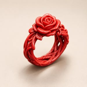 May include: A bright red ring featuring a sculpted rose flower as the central focal point. The band of the ring is crafted with an intricate, interwoven vine and leaf pattern that wraps around the finger, creating a continuous, detailed design.