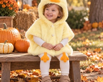 May include: A yellow faux fur hooded cape featuring a duck face on the hood with an orange beak and eyes. The cape has two white pearl-like buttons at the front. Attached to the hem are two orange felt duck feet. The cape is worn over white leggings.