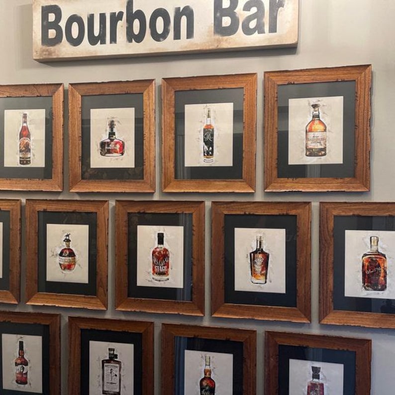 May include: A wall gallery of framed prints featuring various bourbon bottles. The prints are in brown wood frames with black mats. The gallery is titled "Bourbon Bar" in black letters on a white background.