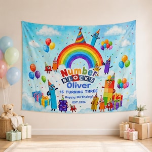 May include: A rectangular fabric wall tapestry featuring a blue sky background with clouds, a rainbow, and colorful cartoon block characters wearing party hats. The text reads Numberblocks Oliver IS TURNING THREE Happy Birthday! EST.2026.