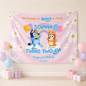 May include: A pink fabric backdrop featuring white daisy flowers, a rainbow, and the cartoon characters Bluey and Bingo. Text reads: THIS EPISODE OF BLUEY IS TITLED SOPHIA TURNS TWO-EY! Happy birthday! EST.2026. Balloons and gift boxes are visible.