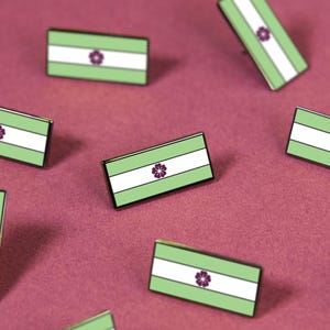May include: A collection of rectangular enamel pins featuring a horizontal tricolor design of light green, white, and light green stripes. Each pin displays a small, dark purple flower icon centered within the white stripe on the front surface.