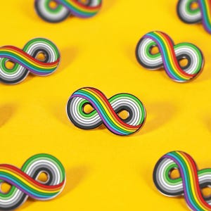 May include: Multiple enamel pins shaped like infinity symbols arranged in a pattern. Each pin features a series of concentric rings in rainbow colors including red, orange, yellow, green, blue, and purple, surrounding a central gray and white core.