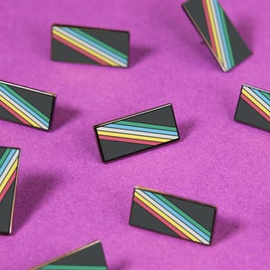 Peut inclure: Une collection d'épinglettes rectangulaires en émail, chacune présentant un fond noir avec un motif de rayures diagonales composé de fines lignes jaunes, bleu clair, blanches et rouges. Les épinglettes sont dispersées dans le cadre.