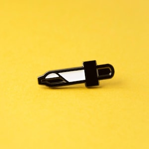 May include: A small enamel pin shaped like a laboratory dropper. The pin features a black metal outline and a white enamel fill, depicting the tapered tip and the bulbous top section of a standard liquid dropper tool used in scientific settings.