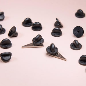 May include: A collection of black rubber pin backs scattered across the frame, with two silver-toned triangular metal pin bases visible in the center, each featuring a black rubber clutch attached to the back post for secure fastening.