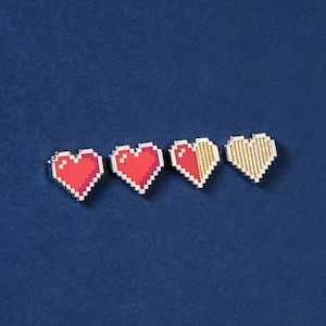 Puede incluir: Cuatro pines de corazones pixelados dispuestos en una fila horizontal. Los dos primeros corazones son de color rojo sólido, el tercero es mitad rojo y mitad dorado, y el cuarto es dorado sólido. Cada corazón presenta un patrón de cuadrícula.
