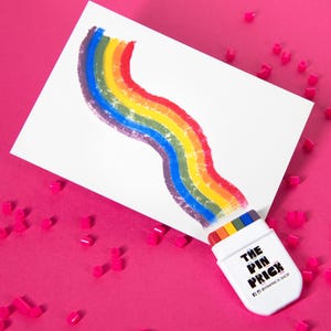 Pode incluir: Um cartão retangular branco com um gráfico ondulado de arco-íris, preso a um suporte de pin de plástico branco. O suporte exibe o texto preto THE PIN PRICK e inclui um pequeno detalhe com as cores do arco-íris na borda superior.