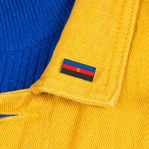 May include: A rectangular enamel pin featuring a horizontal tricolor design of blue, red, and black stripes with a small gold-colored Greek letter pi symbol centered on the red stripe, attached to the collar of a yellow denim jacket.
