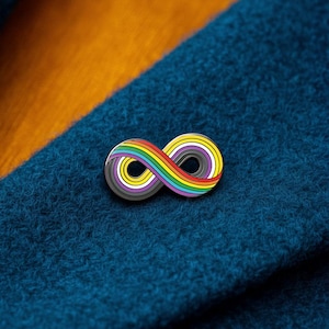 Puede incluir: Un pin de solapa de metal con forma de símbolo de infinito. El diseño presenta un degradado de colores que incluye rojo, naranja, amarillo, verde, azul y morado, que transiciona hacia segmentos de blanco, gris y negro en las líneas curvas.