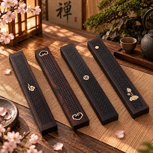 Puede incluir: Cuatro quemadores de incienso rectangulares de madera oscura con intrincados patrones cortados con láser e incrustaciones de metal dorado. Cada quemador presenta motivos decorativos únicos que incluyen nubes, una moneda circular y una flor de loto.