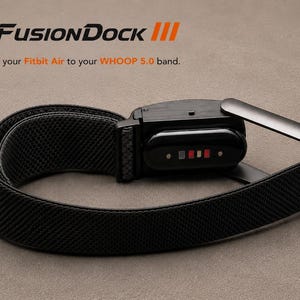 May include: A black FusionDock III adapter for a Fitbit Air on a black WHOOP 5.0 band. The device features a black housing with a sensor array showing four small rectangular contact points in gray, white, and red colors on the underside.