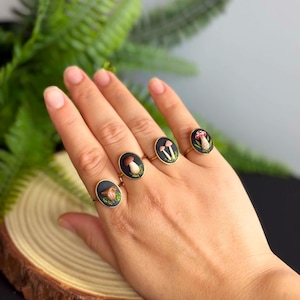 May include: Four gold-toned rings featuring oval black settings, each decorated with a miniature sculpted mushroom design. The rings display various mushroom species, including a brown cap, a tan pair, and a red-capped mushroom with white spots.