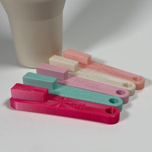 May include: A set of four plastic handle attachments in pink, teal, mauve, and cream, each featuring a rectangular block at one end, a circular hole at the other, and the embossed text "jugforce" with "jugright" or "jugsight" on the surface.