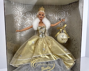 May include: A Celebration Barbie doll from the Special 2000 Edition, wearing a gold glittery gown with snowflake accents, a white faux fur collar, and a gold crown. The doll holds a round, glittery ornament with the year 2000 printed on it.