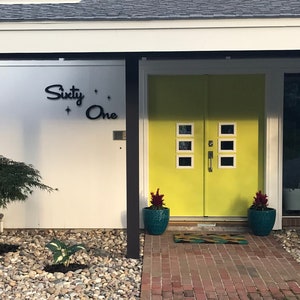 May include: A modern home with a yellow double door and a white exterior. The house number is "Sixty-One" in black lettering. The front yard has a small tree and a brick walkway.