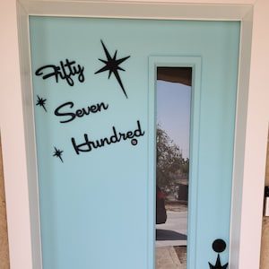 May include: A light blue door with a white frame and a glass window panel. The door has a black starburst design and the text "Fifty Seven Hundred" written on it.