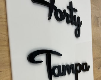 Könnte beinhalten: Schwarzes Acrylschild mit den Worten "Forty Tampa Drive" in einer stilisierten Schriftart.