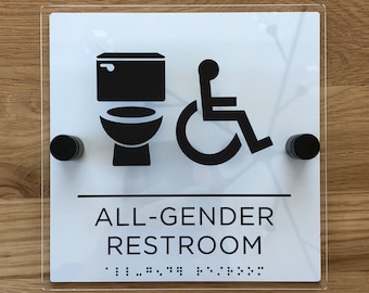 Può includere: Un cartello quadrato bianco con icone nere di un gabinetto e una sedia a rotelle, e le parole "ALL-GENDER RESTROOM" in testo nero. Il cartello include anche testo in braille. Montato con elementi di fissaggio circolari neri.