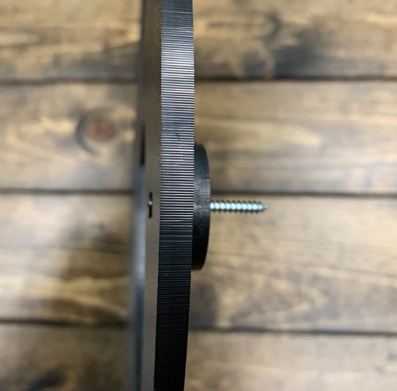 May include: Black metal disc with a textured edge and a screw in the center. The disc is mounted on a wooden surface.