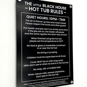 Può includere: Un cartello rettangolare nero con testo bianco, intitolato "THE LITTLE BLACK HOUSE - HOT TUB RULES". Il cartello elenca le regole, tra cui orari di silenzio, impostazioni della temperatura e linee guida di sicurezza. Il cartello è montato con quattro viti argentate.
