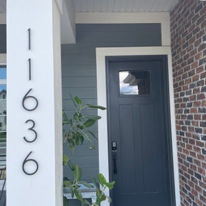 May include: A white house with a black door and a black brick accent wall. The house number 11636 is displayed on the white column.