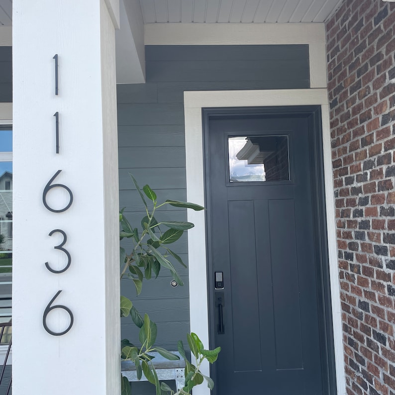 May include: A white house with a black door and a black brick accent wall. The house number 11636 is displayed on the white column.
