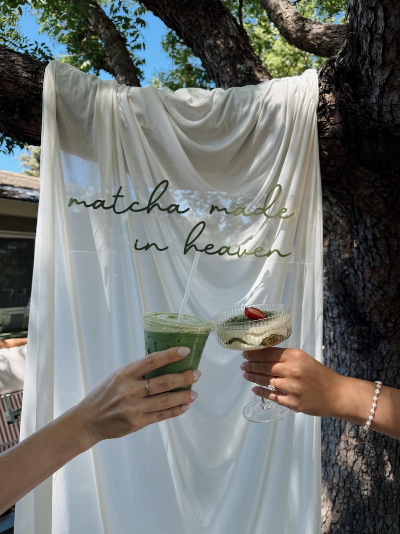 K&ouml;nnte beinhalten: Ein durchsichtiger Plastikbecher mit einem gr&uuml;nen Matcha-Getr&auml;nk und eine gerippte Glasschale mit einem geschichteten Dessert, das mit einer Erdbeere garniert ist, vor einem wei&szlig;en Stoffhintergrund mit dem Text matcha made in heaven.