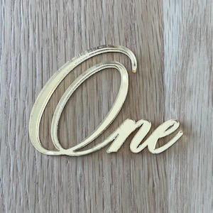May include: Gold mirrored acrylic 'One' cutout, perfect for a first birthday party or other special occasion.