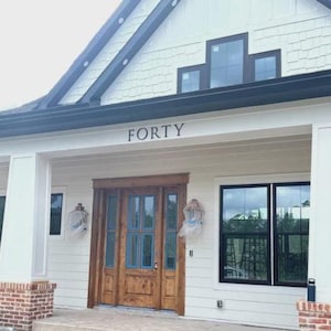 K&ouml;nnte beinhalten: Ein wei&szlig;es Haus mit schwarzen Verzierungen und einer Holzt&uuml;r. Die Hausnummer "FORTY" ist &uuml;ber der T&uuml;r angebracht.