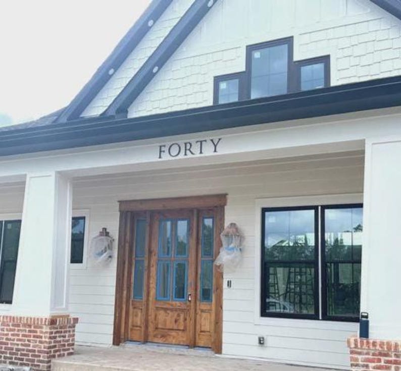K&ouml;nnte beinhalten: Ein wei&szlig;es Haus mit schwarzen Verzierungen und einer Holzt&uuml;r. Die Hausnummer "FORTY" ist &uuml;ber der T&uuml;r angebracht.